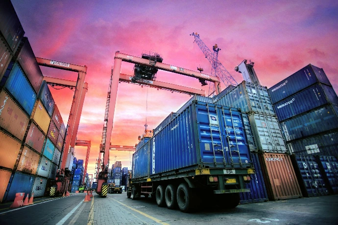 Shipping containers stacked at a busy port at sunset.